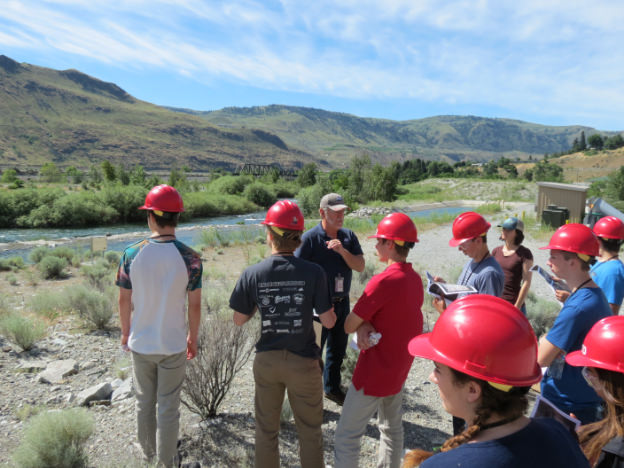 Students in hard-hats listen to tour guide near river